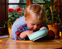Fotografía de un niño pequeño comiendo sin ayuda en su silla alta para niños