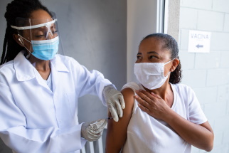 Healthcare provider with a mask and face shielf gives vaccine to masked patient