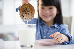 Young girl dunking a cookie in a glass of milk