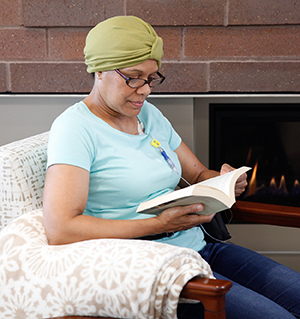 Woman sitting at home reading, with chemo infusion port in chest.