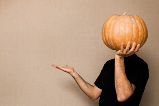 Person holding a large pumpkin in the palm of their hand blocking the view of the person's head